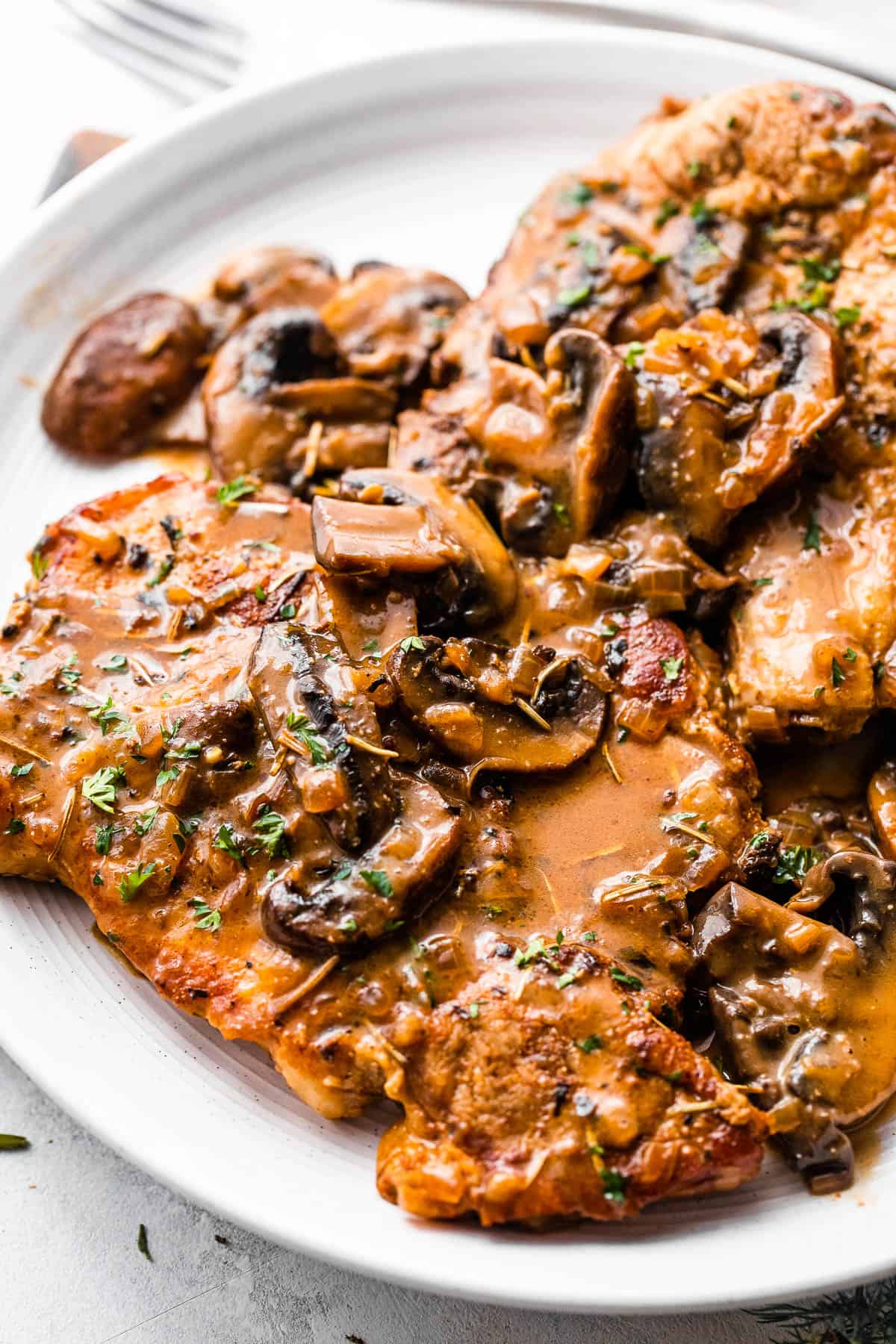 two bone in pork chops served on a white plate and topped with creamy mushroom gravy