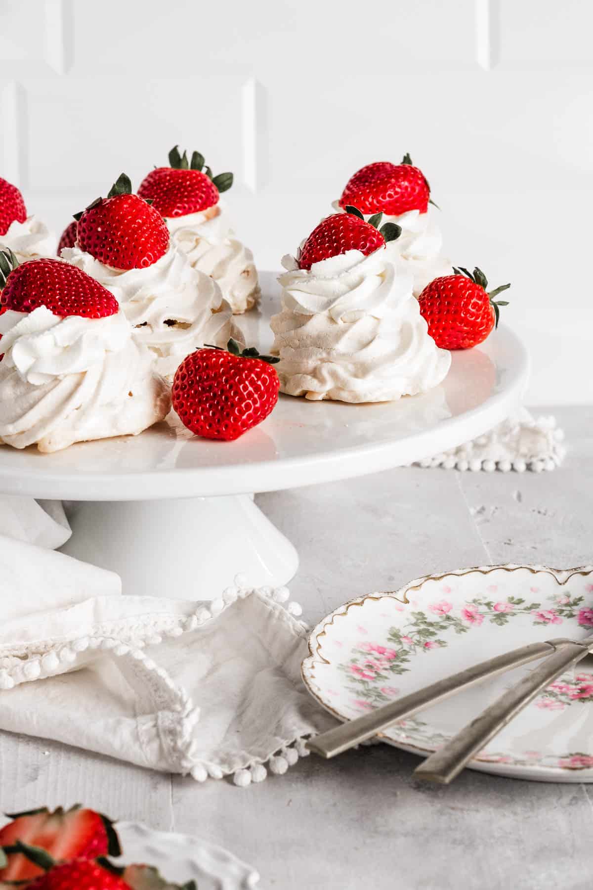 Mini pavlovas on a cake plate topped with whipped cream and strawberries
