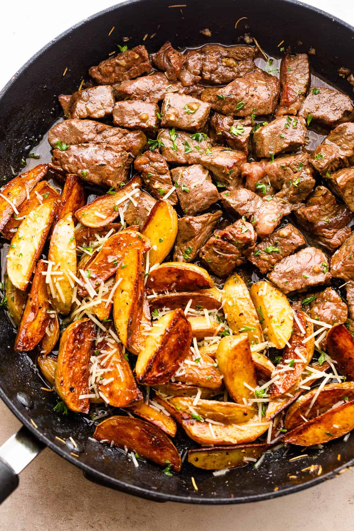 cubed steak and quartered potatoes cooking in a skillet