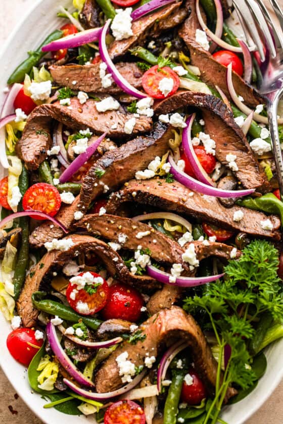 Steak Salad on a long plate topped with cheese crumbles, tomatoes, and mushrooms