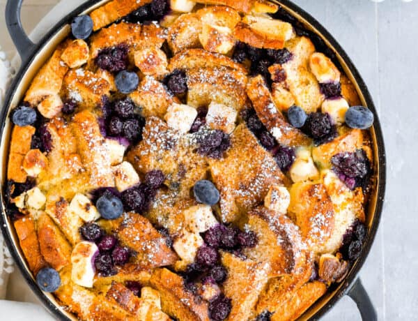 A Bird's-Eye View of a Blueberry French Toast Casserole Beside a Cup of Fresh Blueberries and a Spouted Measuring Cup of Maple Syrup