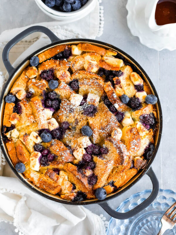 A Bird's-Eye View of a Blueberry French Toast Casserole Beside a Cup of Fresh Blueberries and a Spouted Measuring Cup of Maple Syrup