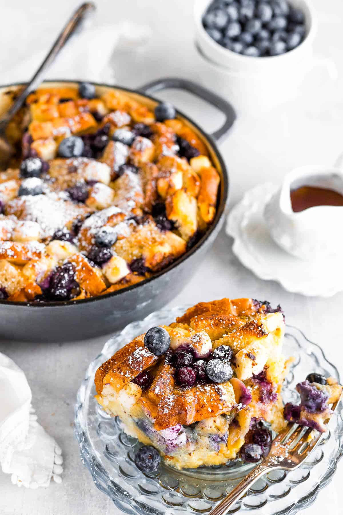 A Serving of Blueberry French Toast Bake on a Plate with the Full Casserole Behind it