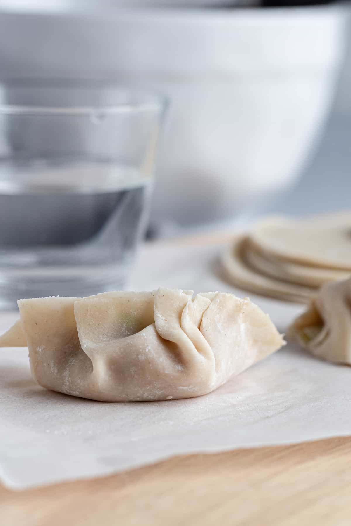 A Filled and Sealed Dumpling Beside a Cup of Water
