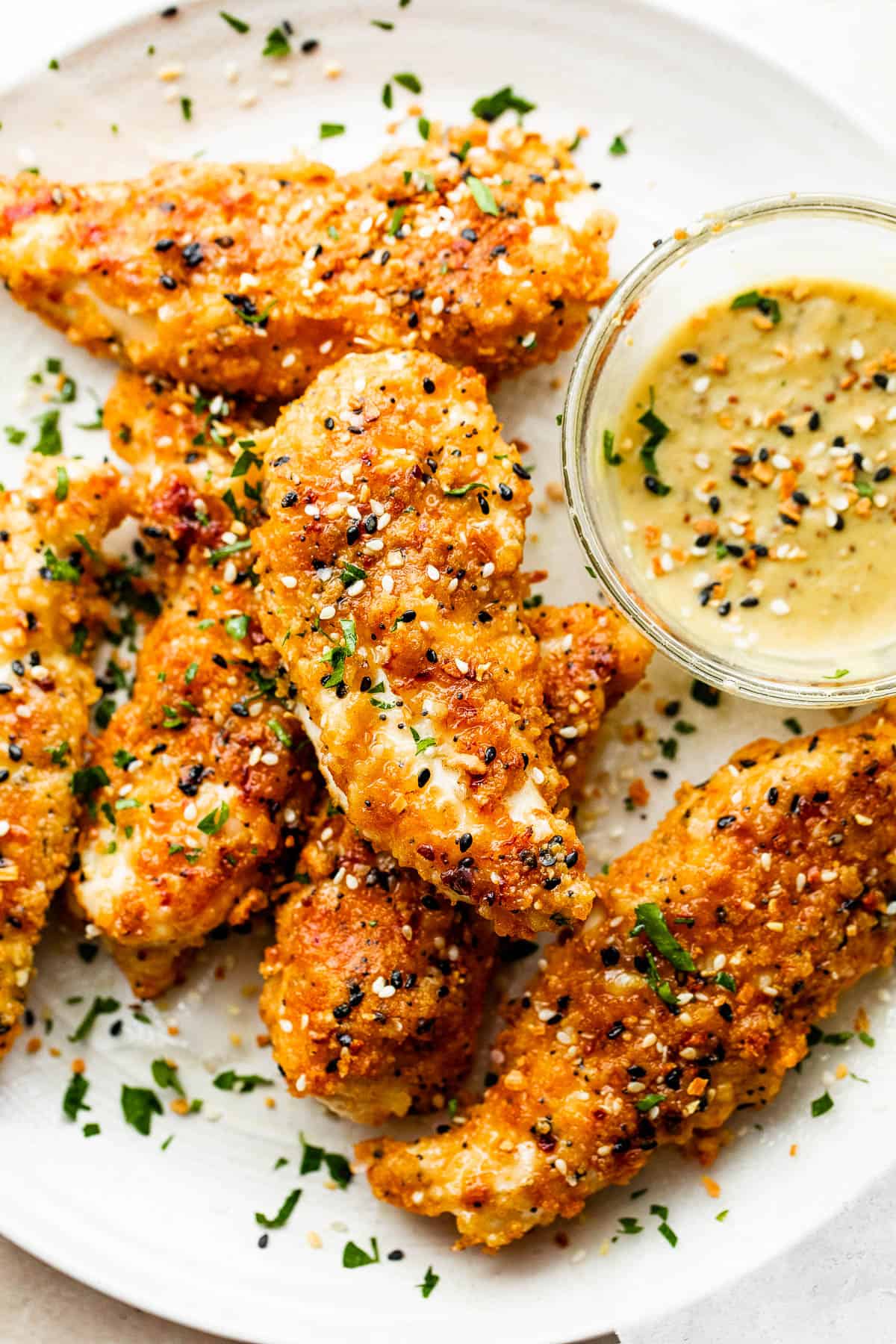 close up of six Everything Bagel Chicken Tenders arranged on a round plate and served with honey mustard dipping sauce