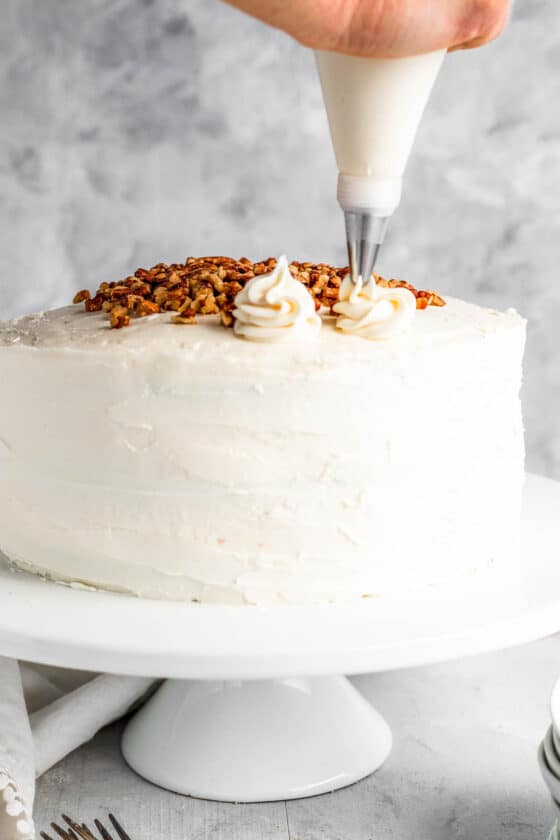 A Piping Tip Adding Swirls of Cream Cheese Icing Onto the Frosted Cake