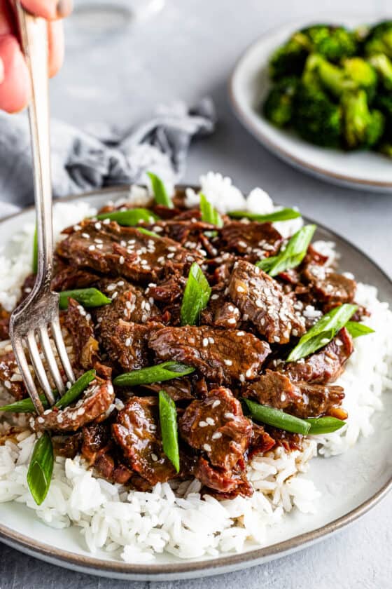 A Metal Fork Digging Into a Plate of Instant Pot Mongolian Beef Over White Rice