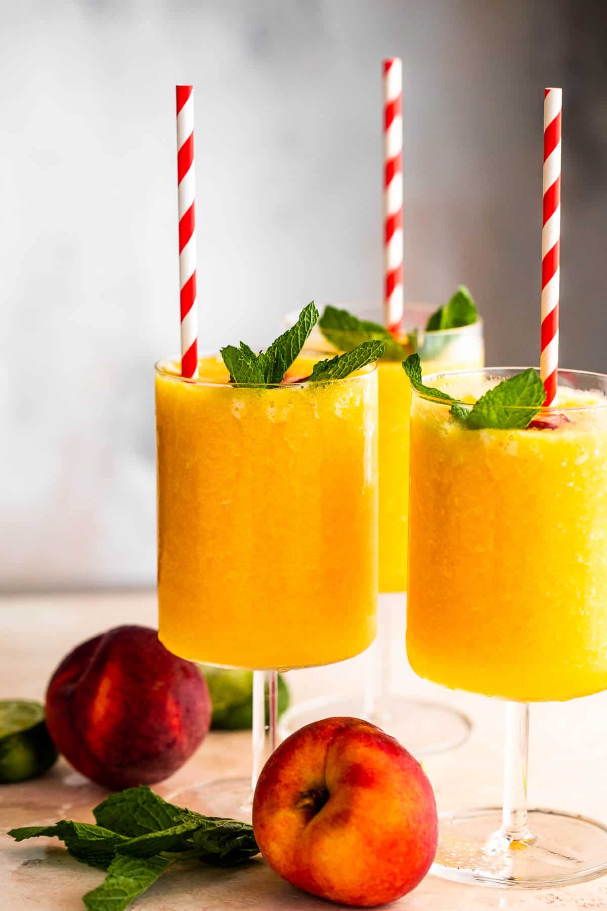 three glasses filled with peach daiquiris and garnished with mint, peach slices, and straws