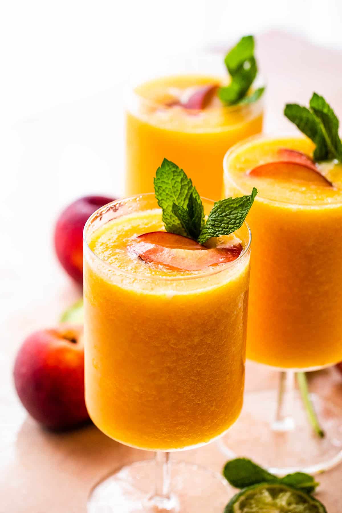 three glasses filled with peach daiquiris and garnished with mint and peach slices