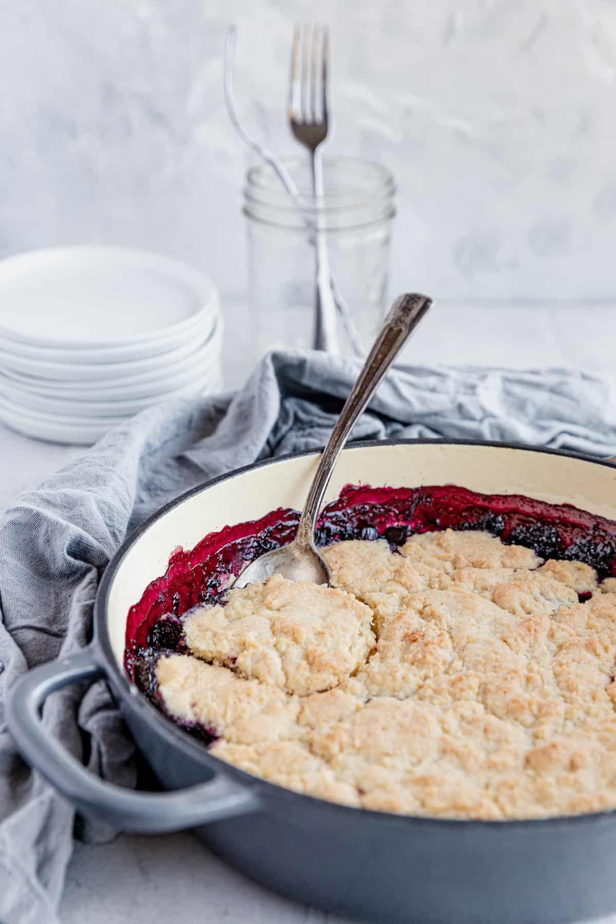 A Freshly Made Blueberry Rhubarb Cobbler in a Pan with a Metal Spoon Digging Into the Dessert