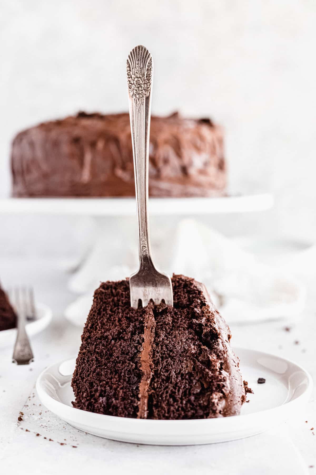A Slice of Chocolate Cake on a White Plate with a Fork Sticking Into it