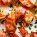 up close photo of bacon wrapped shrimp arranged on a white plate and garnished with parsley