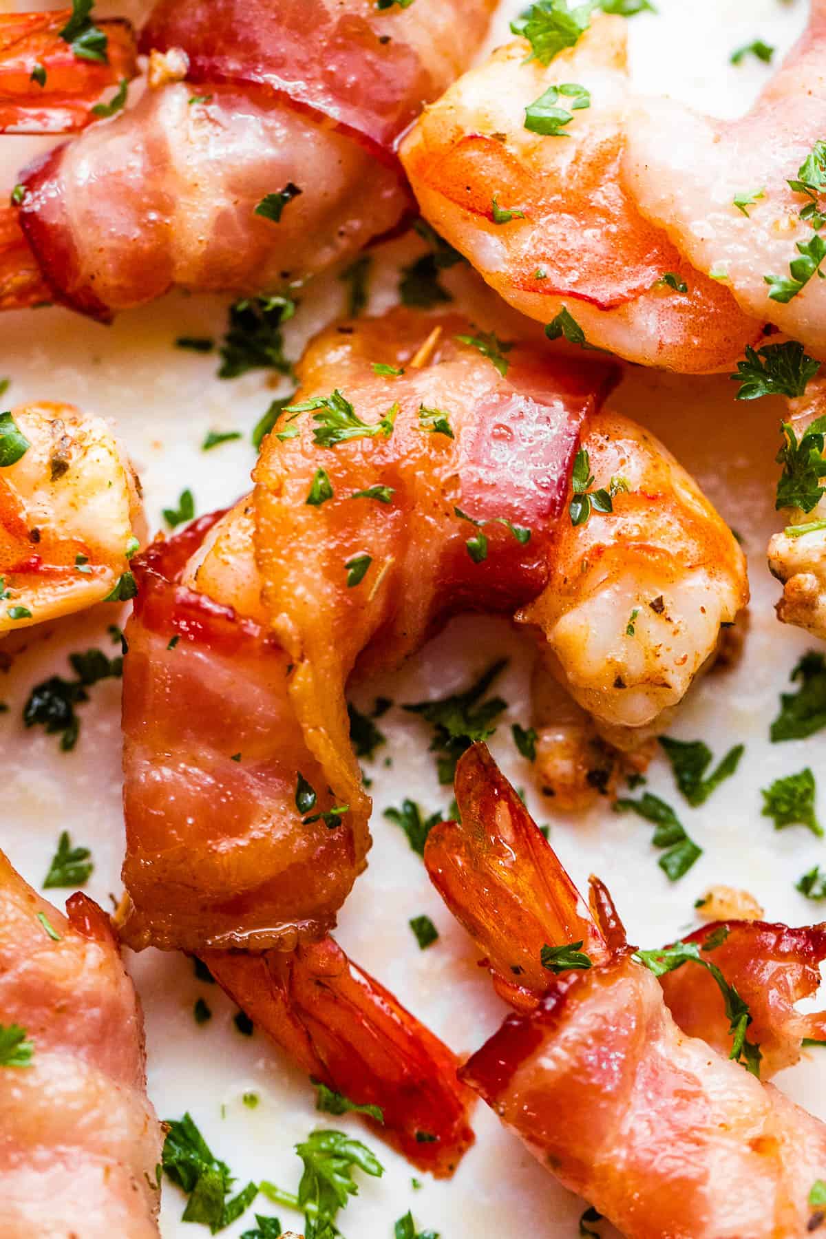 up close photo of bacon wrapped shrimp arranged on a white plate and garnished with parsley