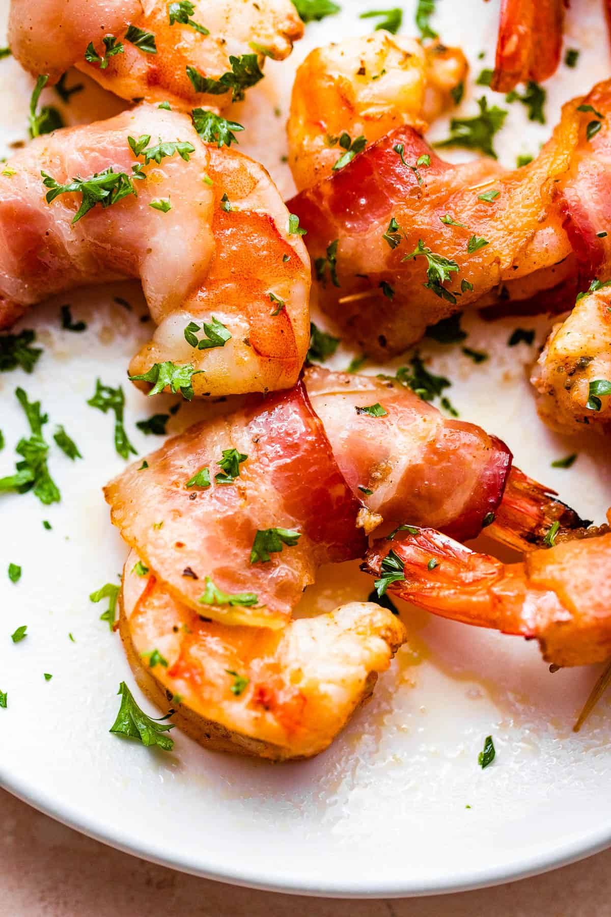 bacon wrapped shrimp arranged on a white serving plate and garnished with parsley