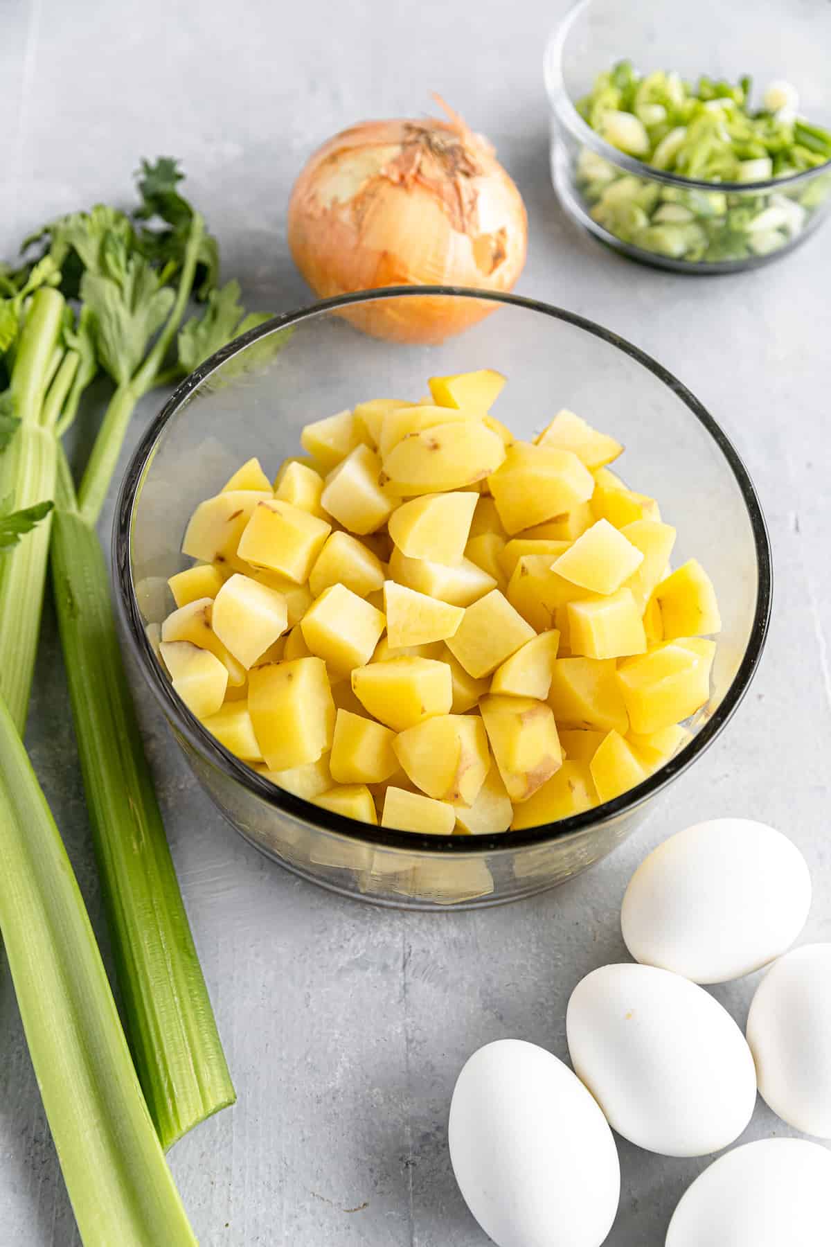 Chopped Potatoes, Hard-Boiled Eggs, a Yellow Onion and the Rest of the Potato Salad Ingredients on a Gray Countertop