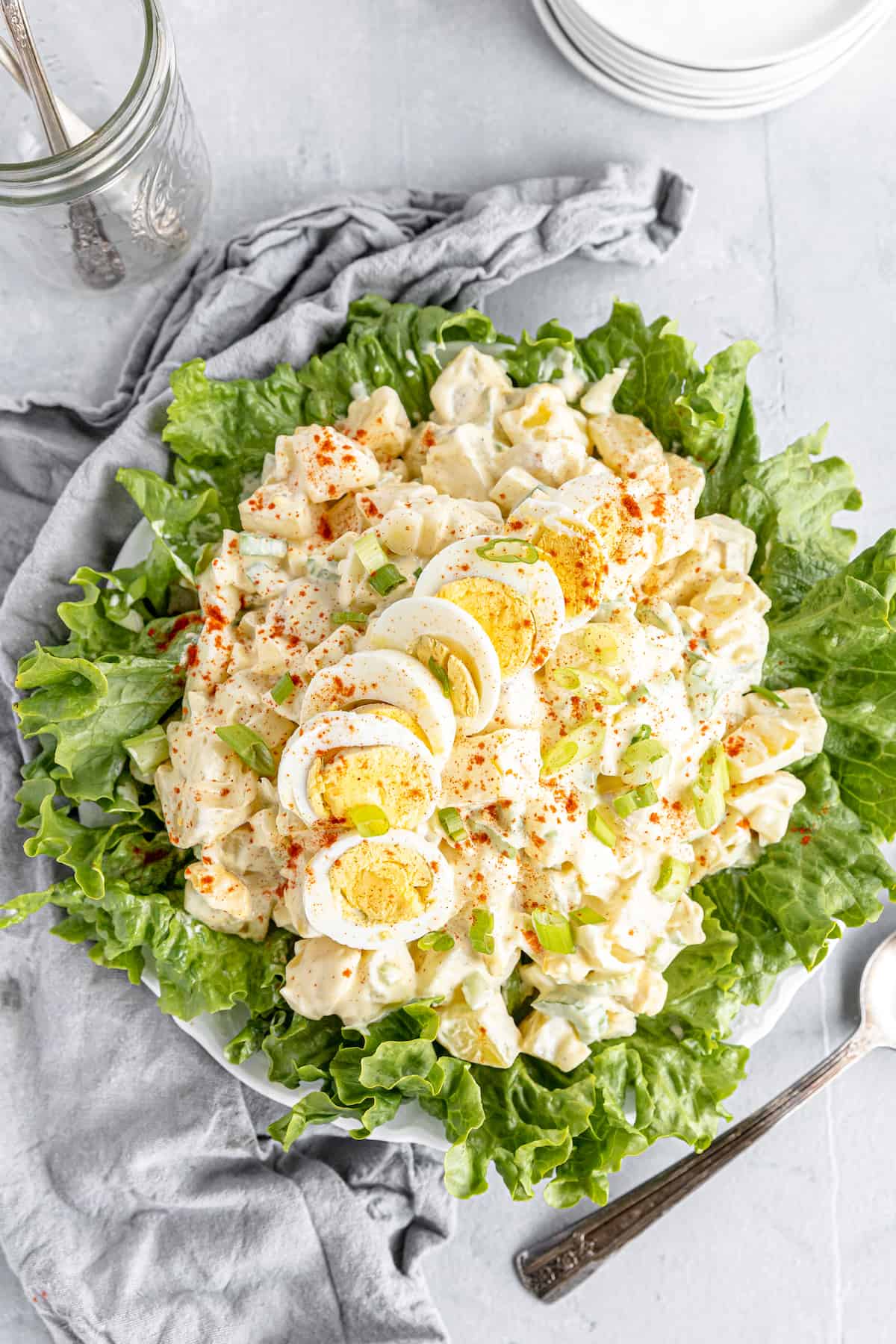 An Overhead Shot of a Potato Salad on a Lettuce-Lined Plate Beside a Gray Kitchen Towel