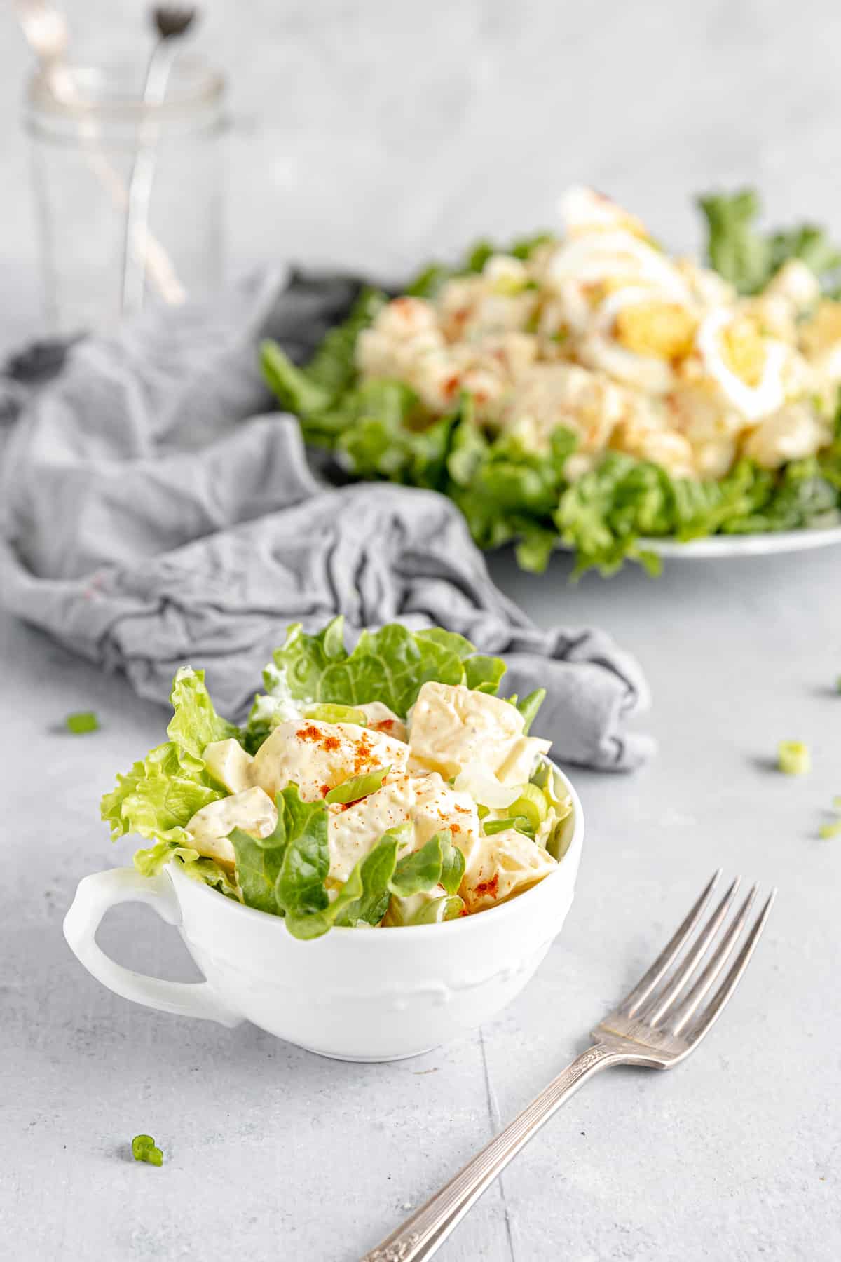 A Serving of Potato Salad in a Mug with the Remaining Salad on a Plate in the Background