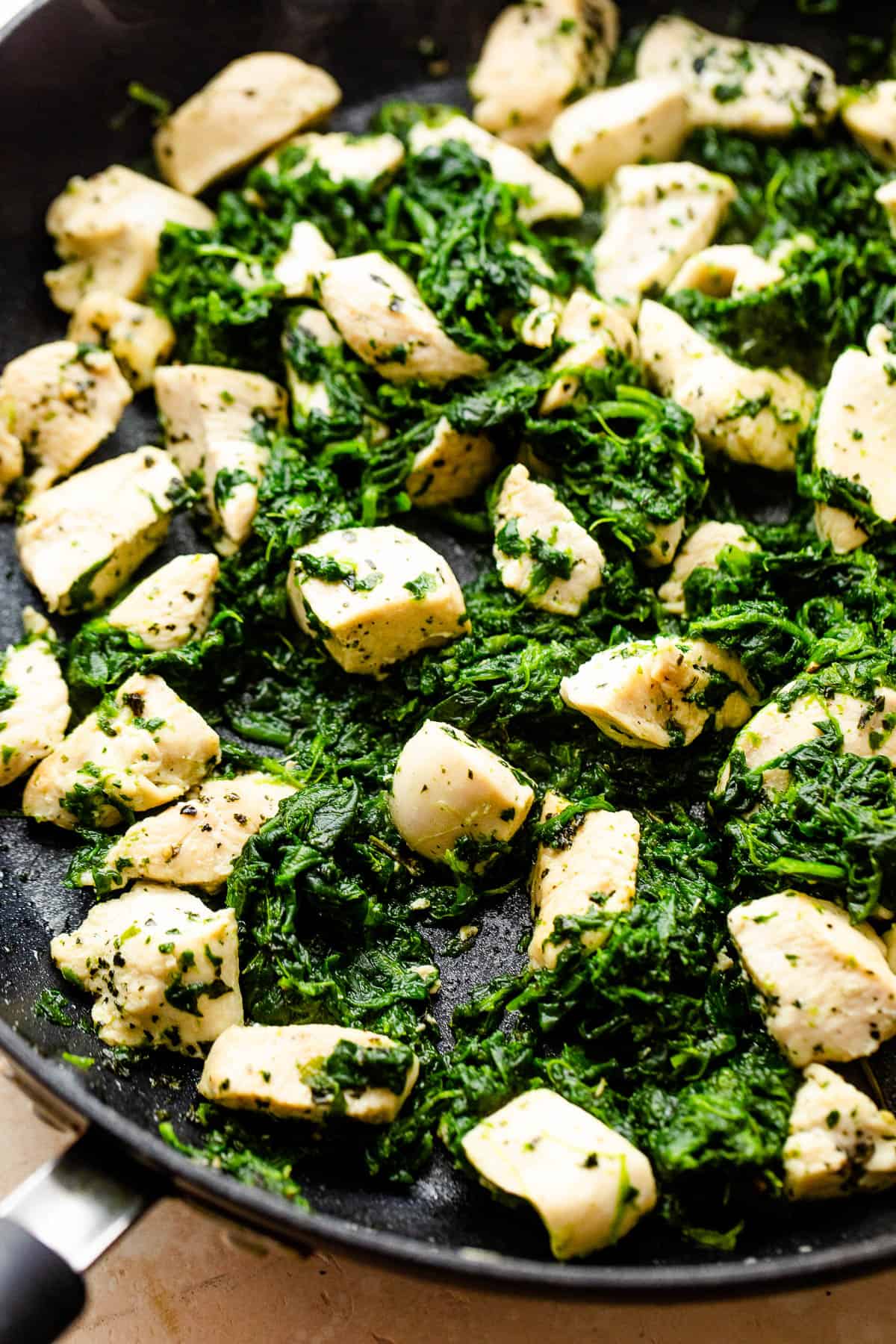 cooking chicken breast pieces and spinach in a black skillet