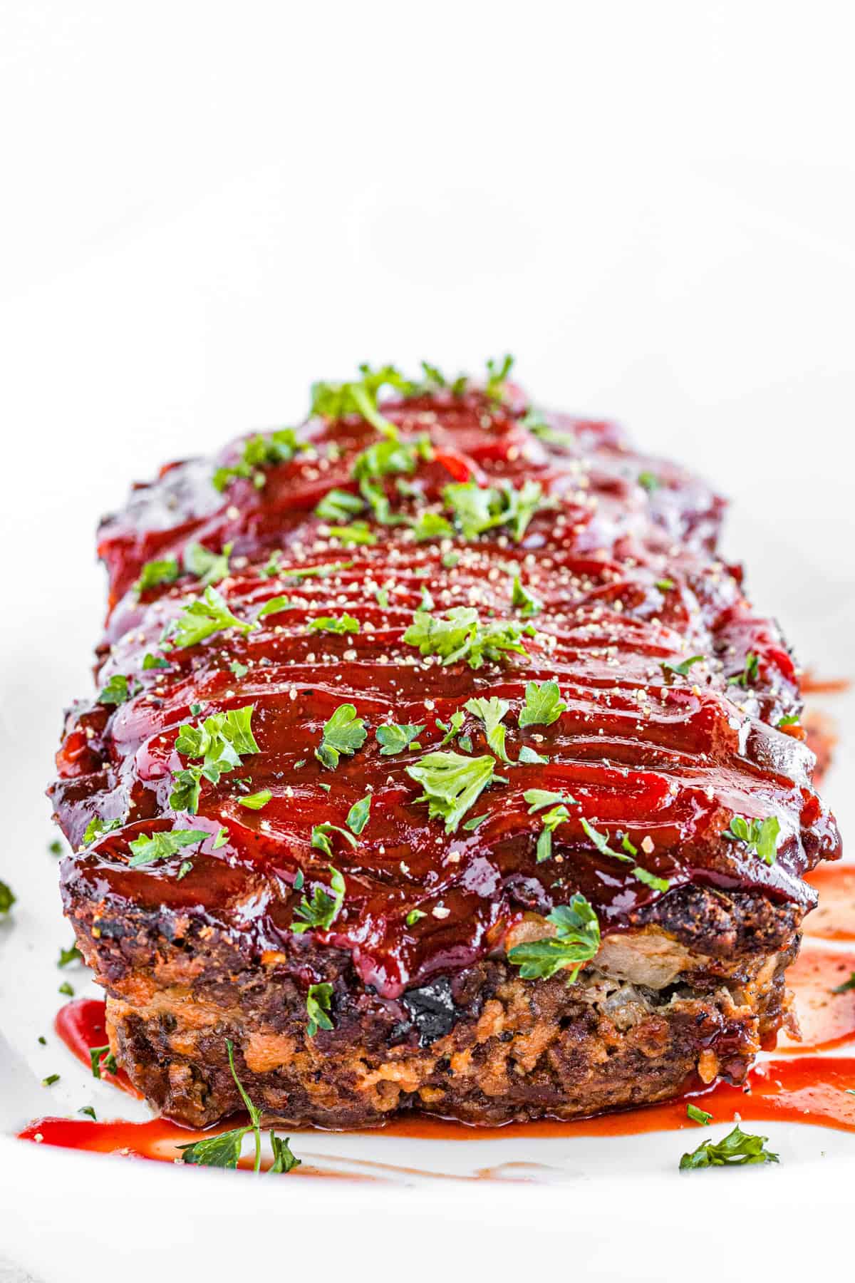 Cooked meatloaf topped with barbecue sauce and chopped fresh parsley.