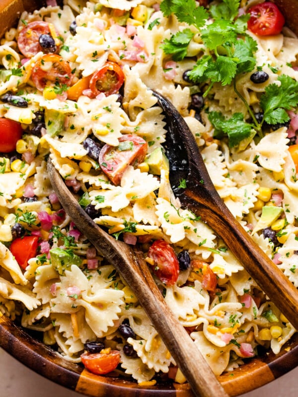 pasta salad in a wooden salad bowl with two wooden spoons