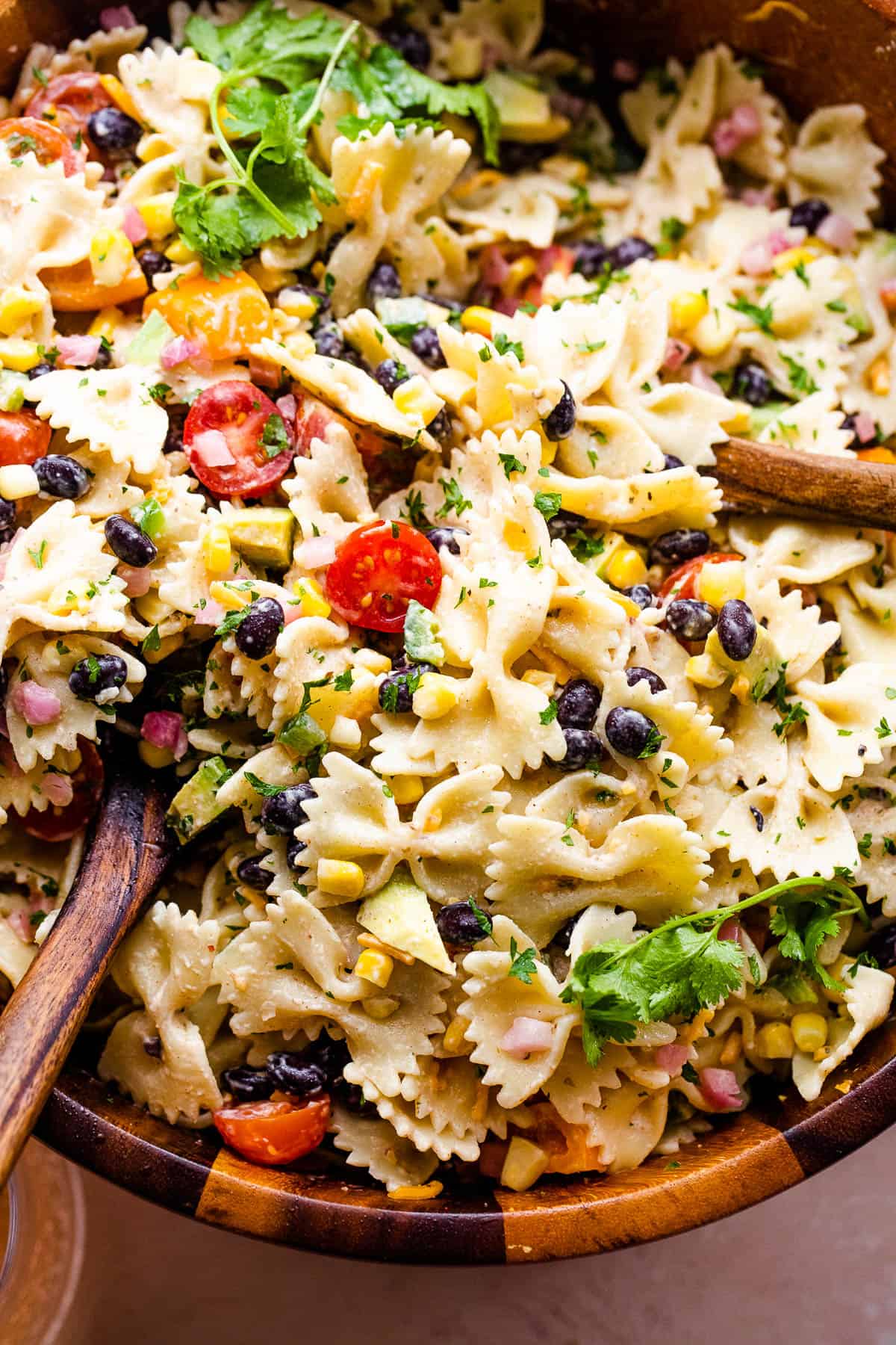 up close shot of fiesta pasta salad in a wooden salad bowl with two wooden spoons