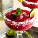 Frozen Berry Margarita served in a margarita glass with salted rims, slice of lime, and mint
