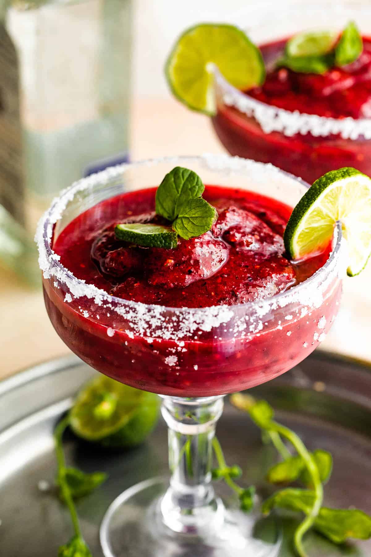 Frozen Berry Margarita served in a margarita glass with salted rims, slice of lime, and mint
