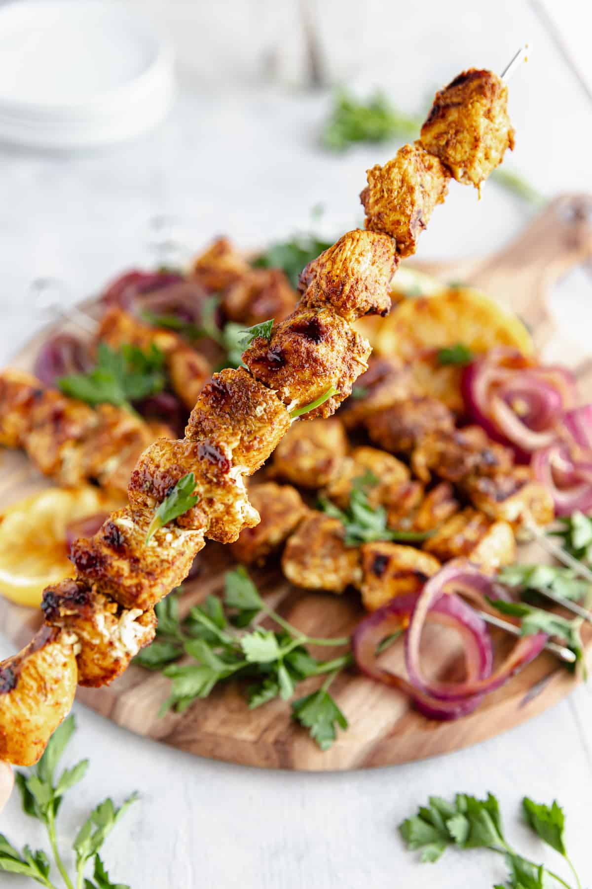 A Shawarma Grilled Chicken Skewer Being Held Above a Platter Containing More Kebabs