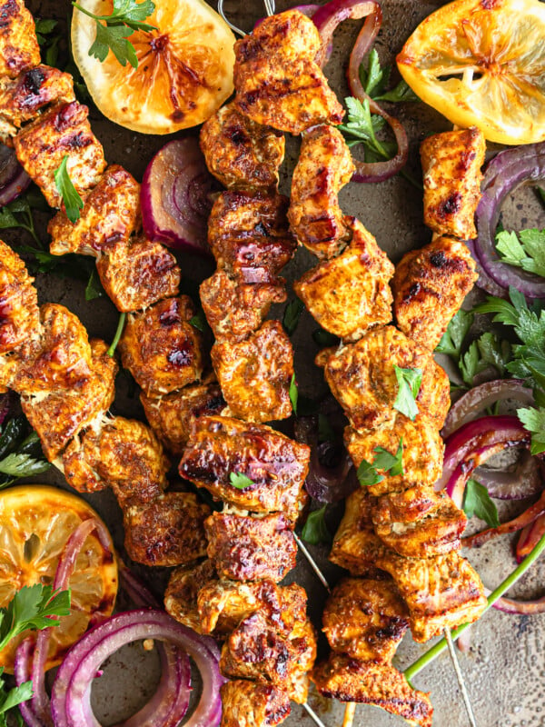Five Shawarma Grilled Chicken Skewers on a Metal Pan with Onions, Lemon Slices and More