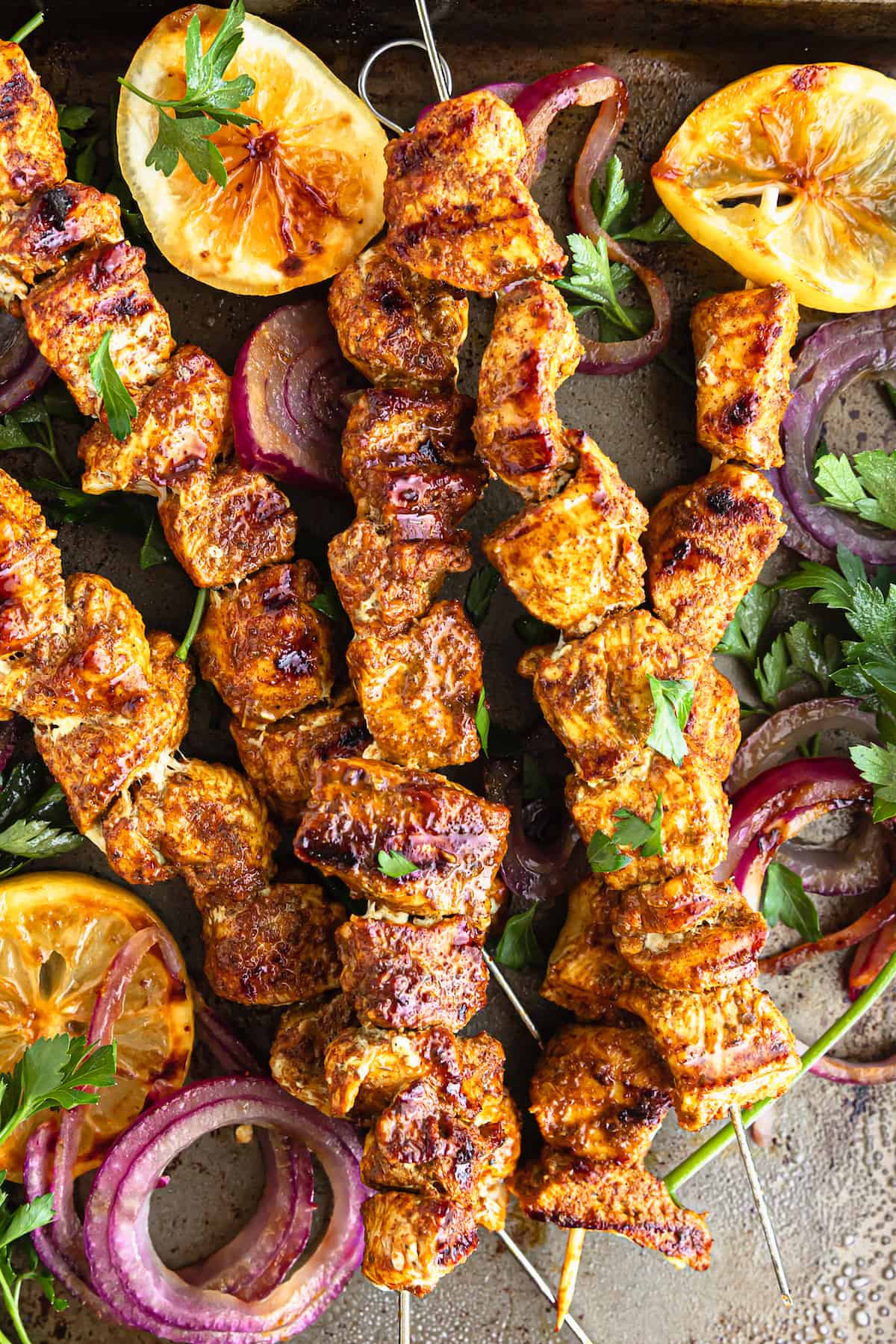 Five Shawarma Grilled Chicken Skewers on a Metal Pan with Onions, Lemon Slices and More