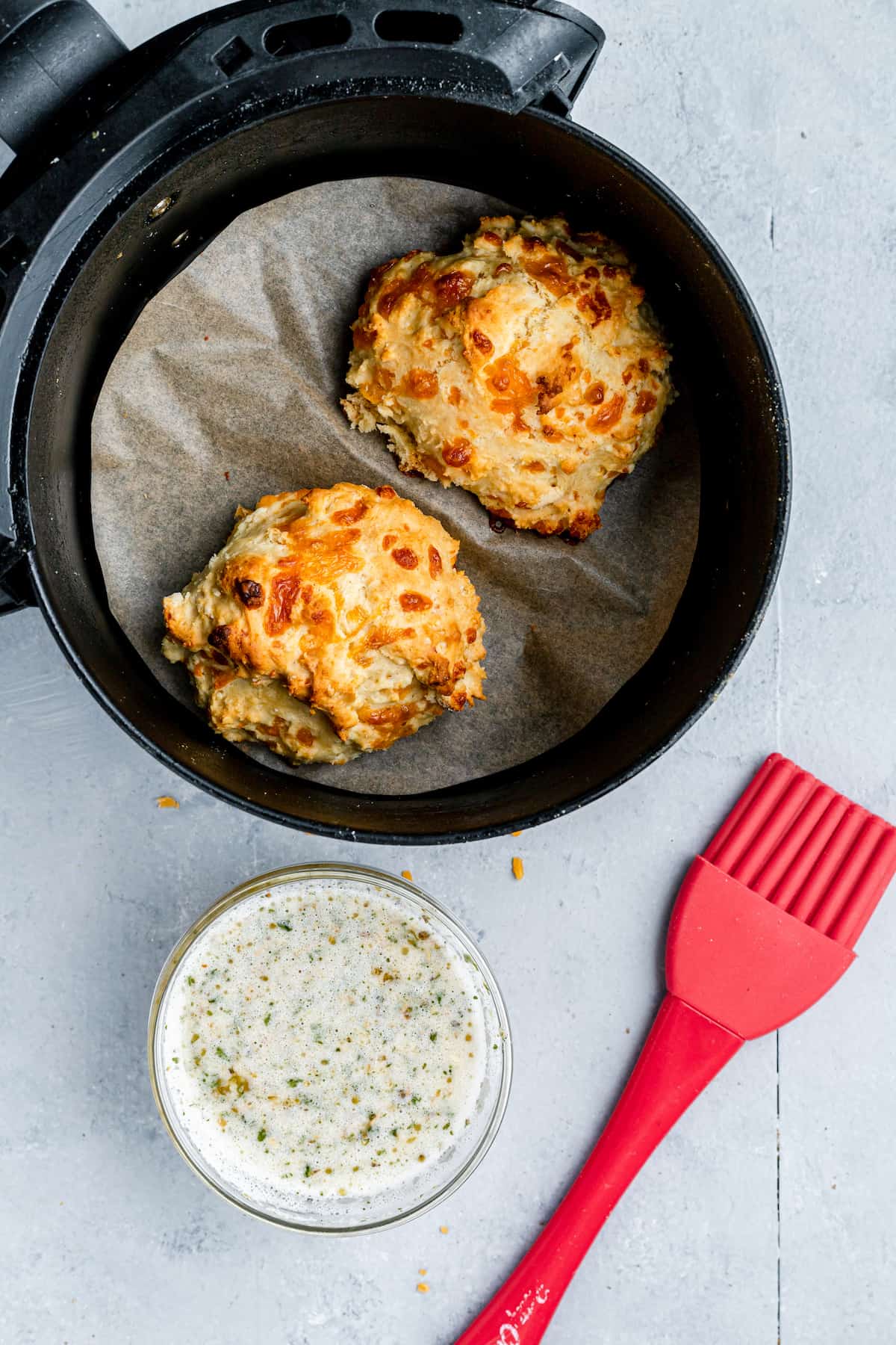 Two Red Lobster Biscuits in an Air Fryer Beside a Dish of Garlic Butter