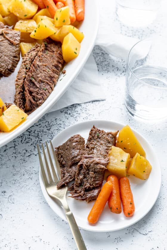 A white plate with pot roast, carrots and potatoes