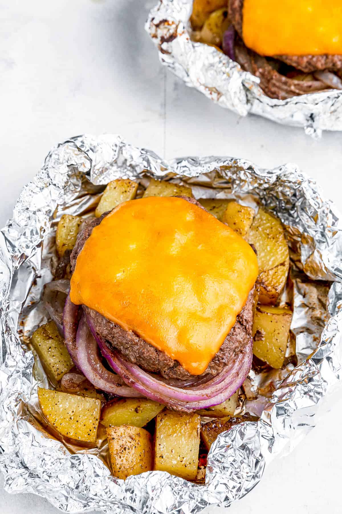 Two cheeseburgers in foil with potatoes