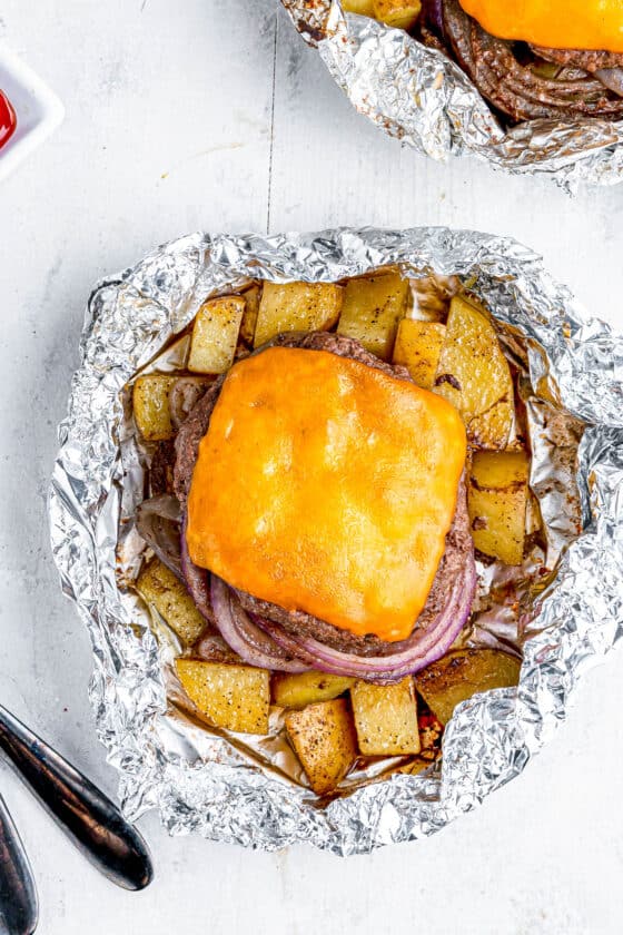 Two cheeseburgers in foil with potatoes