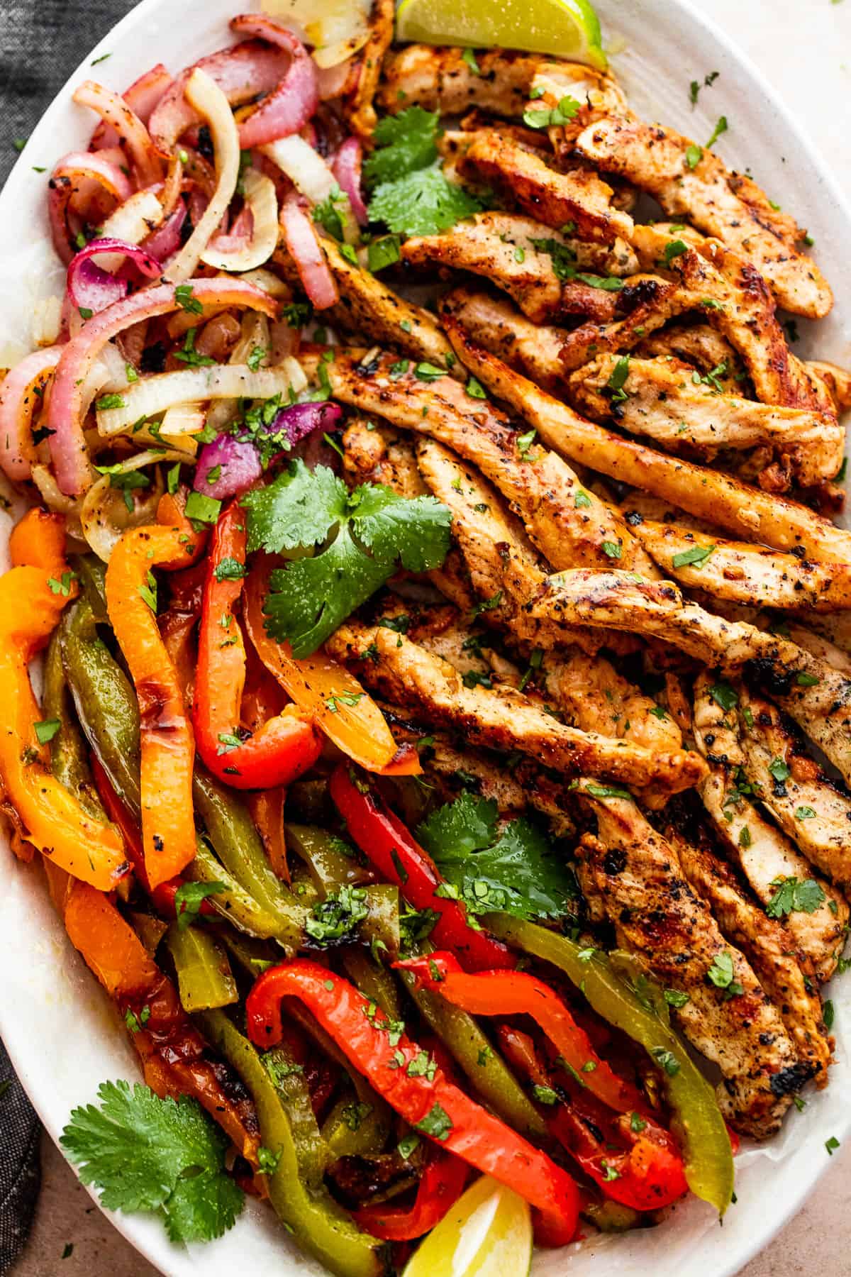 grilled chicken strips, colorful bell pepper strips, and onions on a serving plate garnished with cilantro leaves