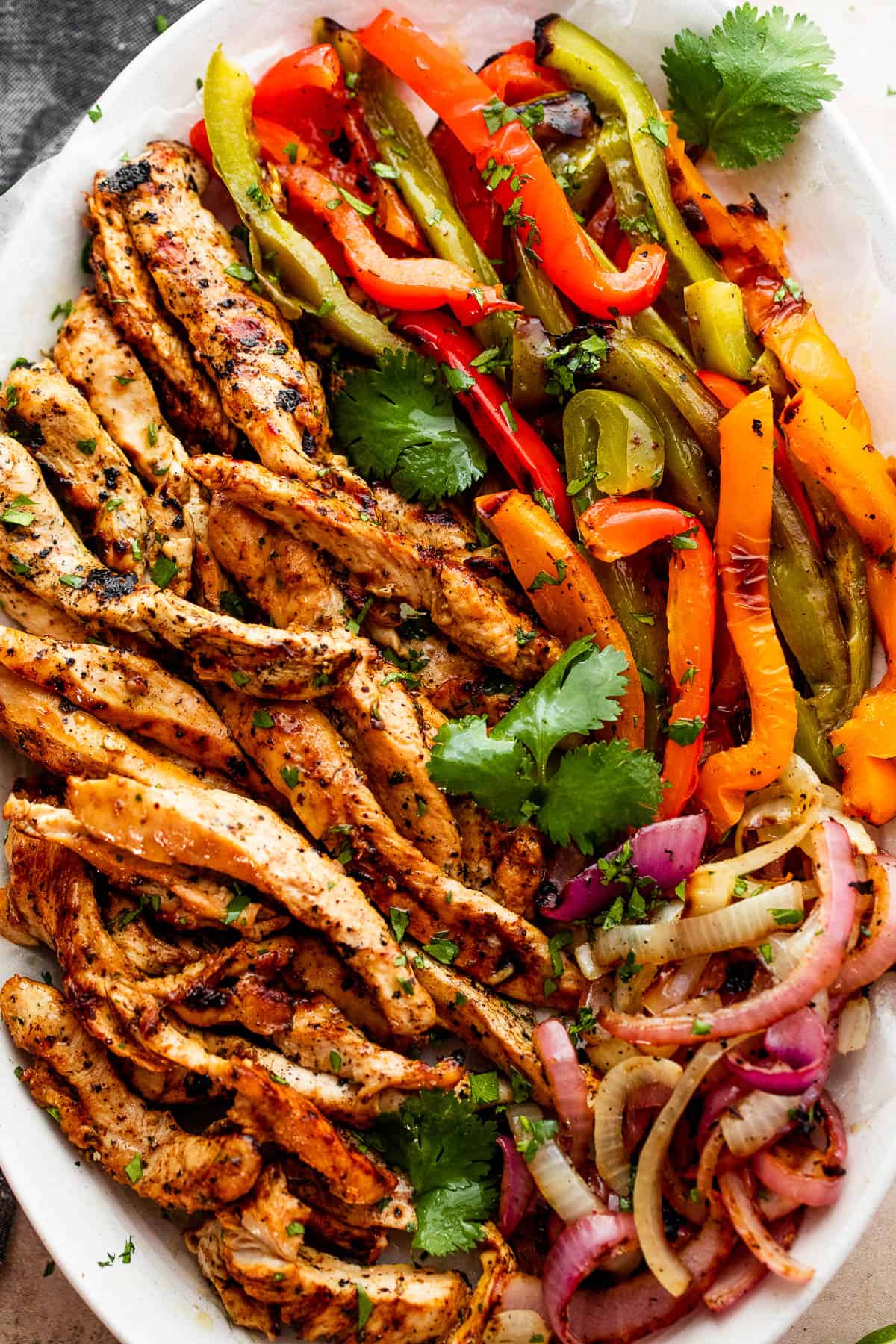 grilled chicken strips, colorful bell pepper strips, and onions on a serving plate garnished with cilantro leaves