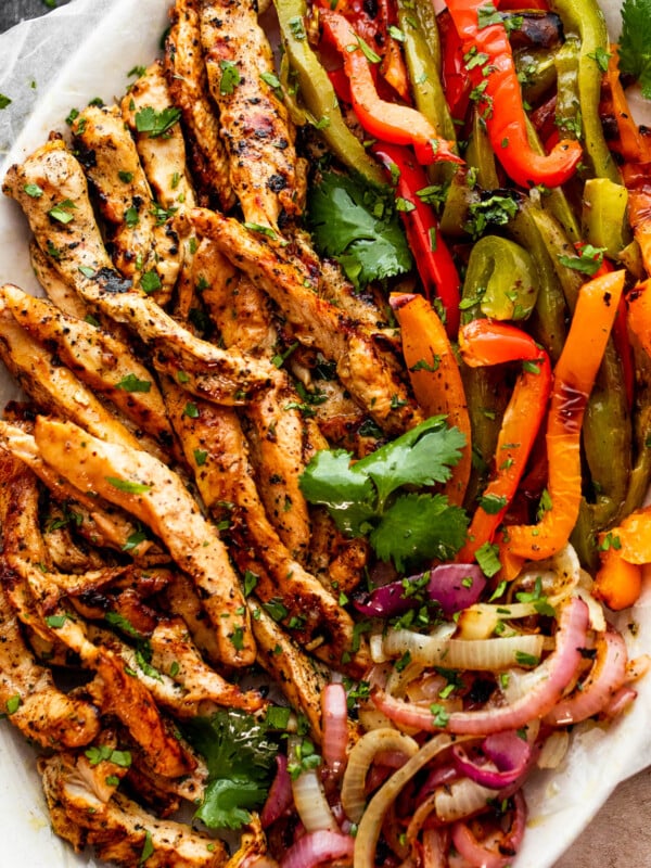 grilled chicken fajitas with chicken strips, colorful bell pepper strips, and onions on a serving plate garnished with cilantro leaves