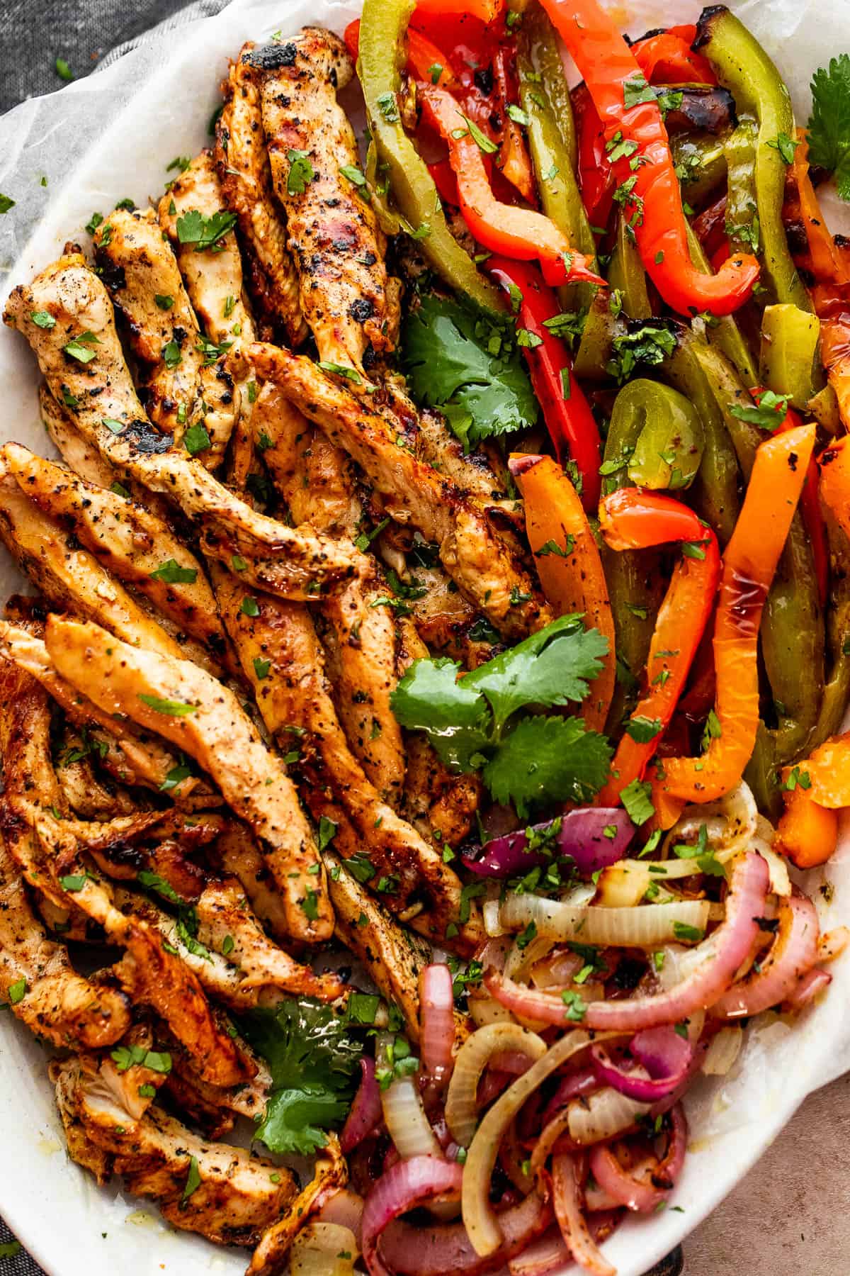 grilled chicken fajitas with chicken strips, colorful bell pepper strips, and onions on a serving plate garnished with cilantro leaves