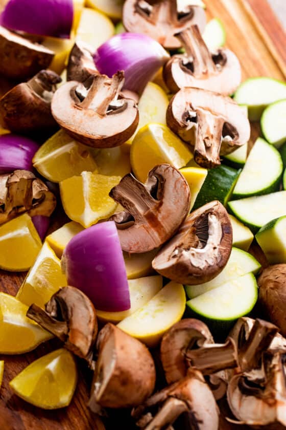 a pile of chopped mushrooms, red onions, lemons, and squash on a wooden board