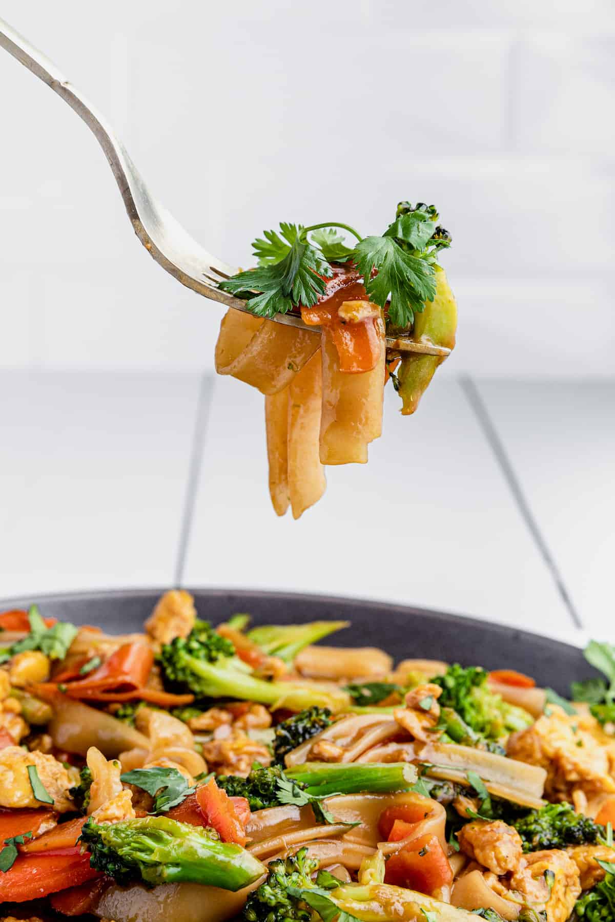 A Bite of Pad See Ew on a Fork Hovering Above a Full Plate