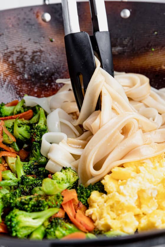A Pair of Tongs Mixing the Noodles with the Eggs and Vegetables