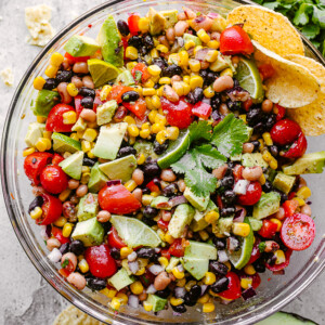 Cowboy caviar with avocado, corn, tomatoes, black-eyed peas, beans and cilantro in a large glass bowl