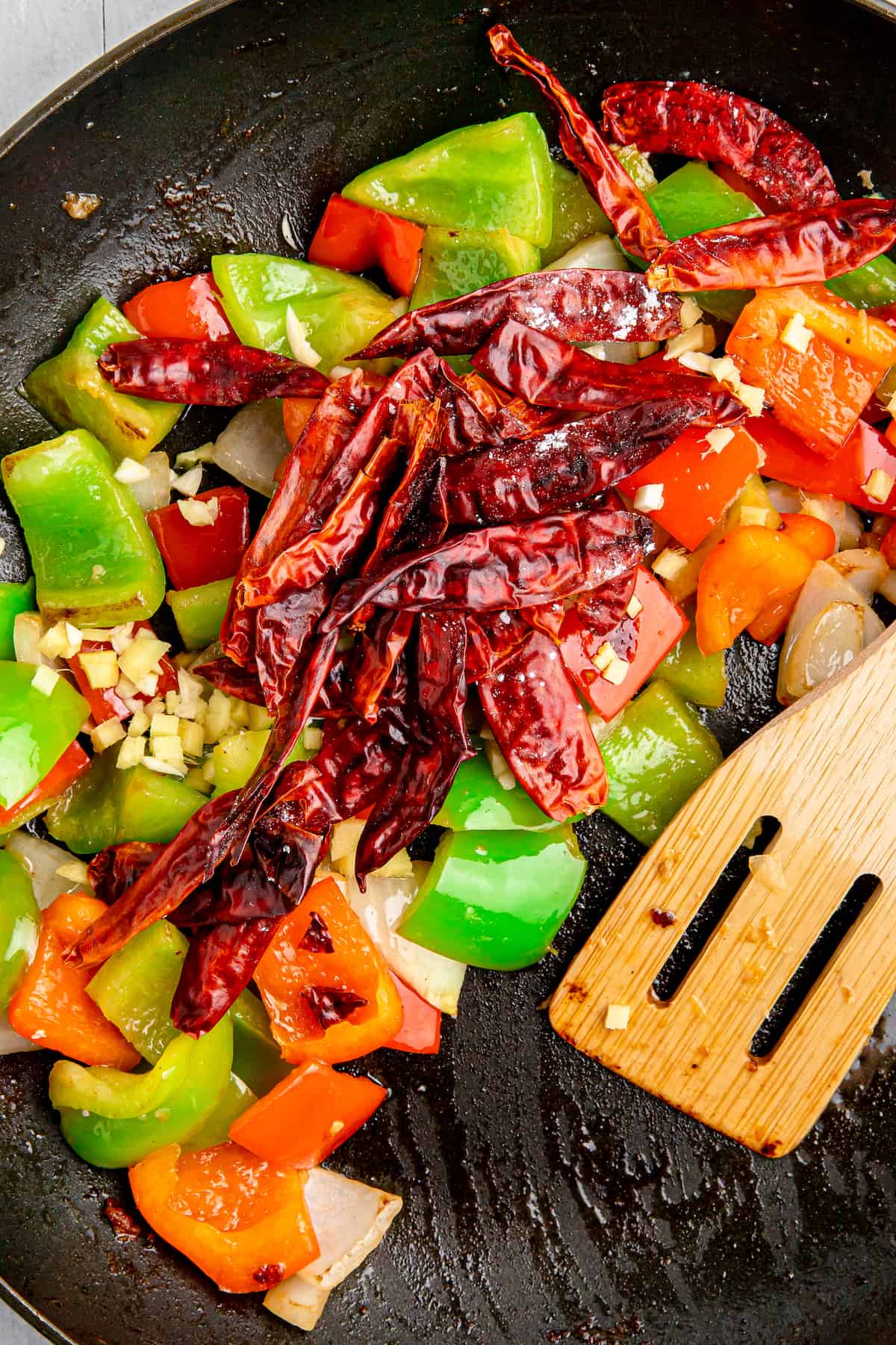 Chopped vegetables and dried chilies are sauteed in a pan.