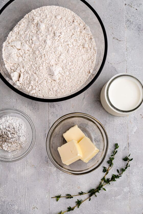 Clockwise from top: all-purpose flour, milk, butter, a sprig of thyme, seasonings and baking powder.