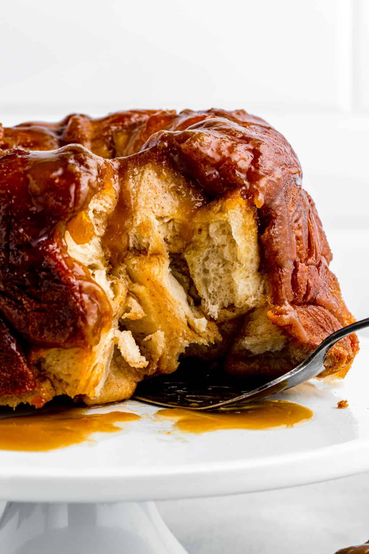 A baked monkey bread on a cake stand has several pieces removed and a cake server tucked underneath it.