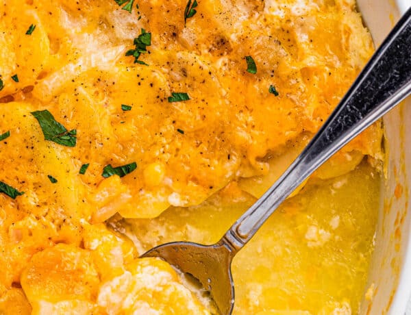 scalloped potatoes in a white casserole dish with a spoon inside the dish