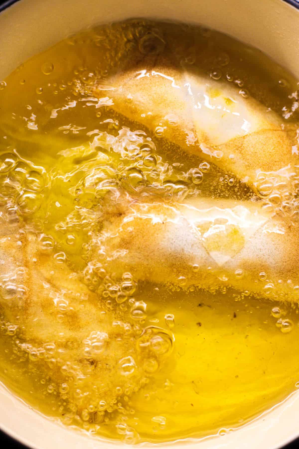 Spring rolls being deep fried in a skillet.