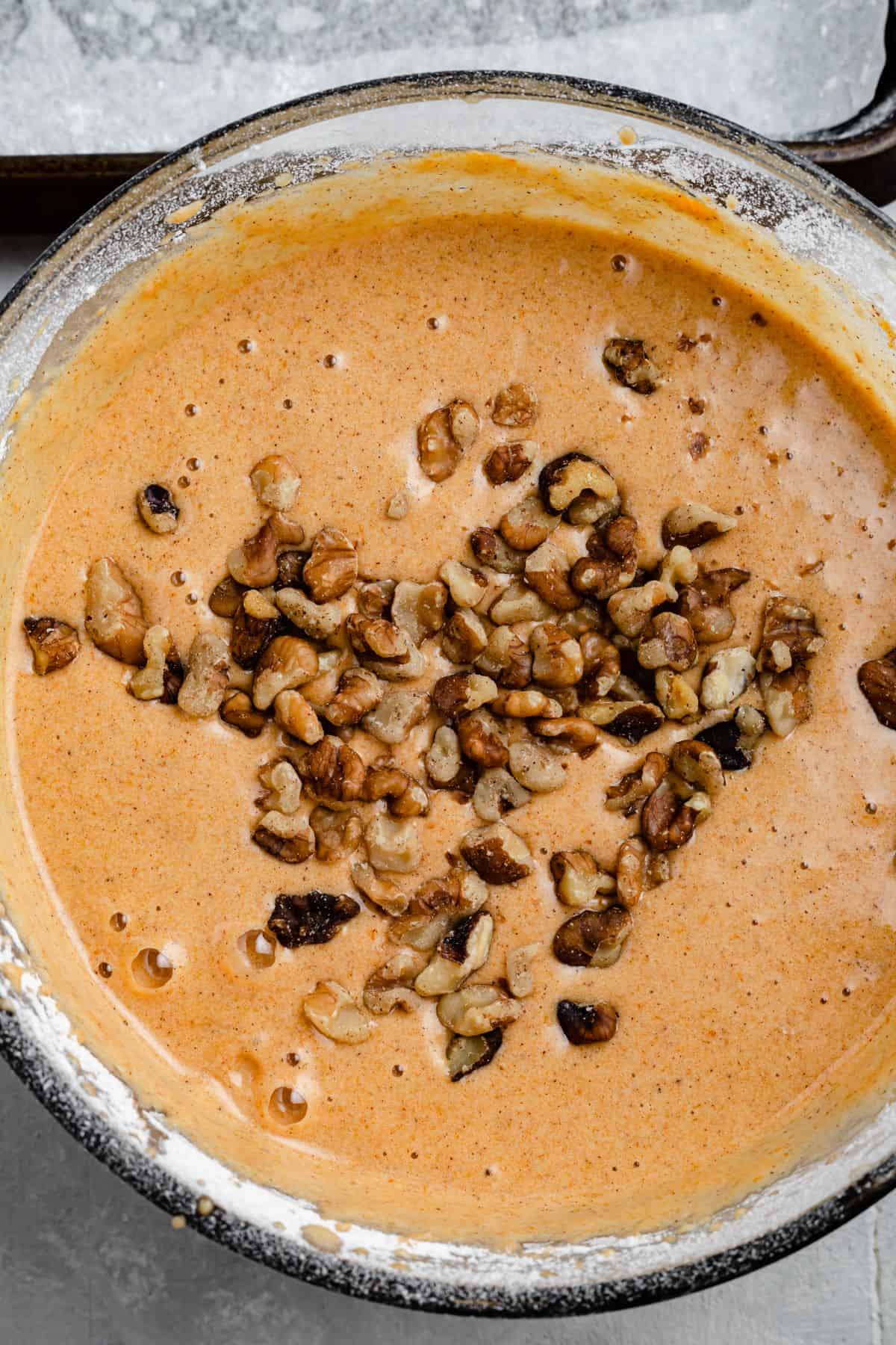 A mixing bowl full of pumpkin cake batter, with chopped walnuts sprinkled on the surface of the batter.