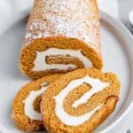 A shot of the pumpkin roll cake, dusted with powdered sugar, with two slices overlapping on a platter.