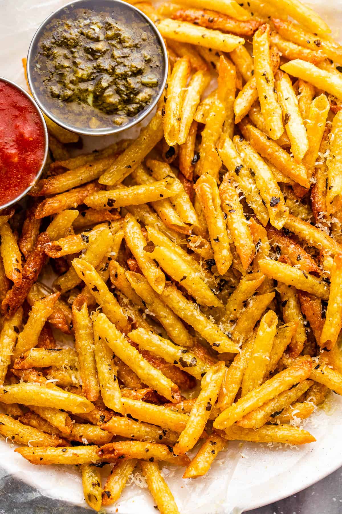 plate with baked pasta chips served with a side of basil pesto and marinara sauce